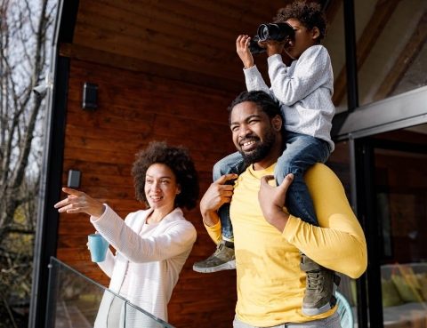 Couple pointing in a direction while a child sits on the mans shoulders with a pair of binoculars