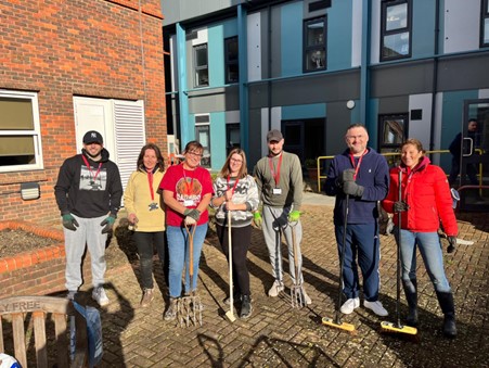 7 adults with gardening tools stood in front of East Surrey Hospital